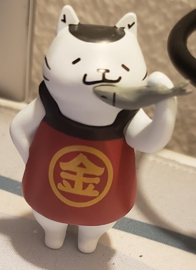 a white cat figurine with an apron eating a fish